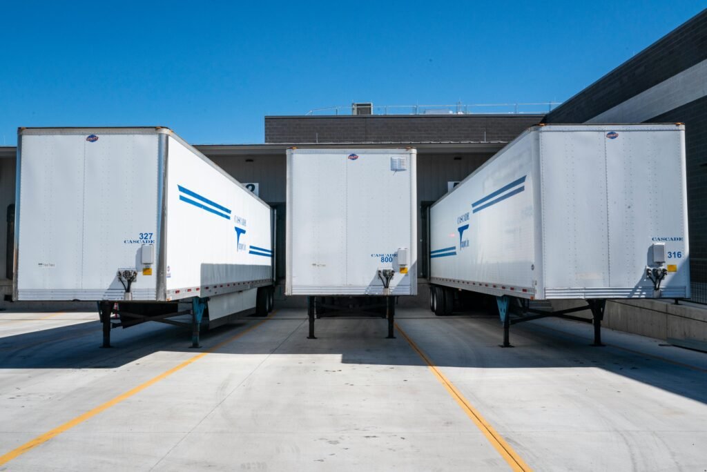 Three white cargo trailers parked at an industrial shipping dock under clear blue skies.